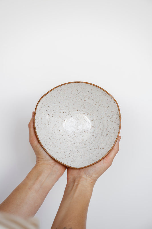 Two hands hold a handmade speckled white Triangle bowl with a round triangular shape against a plain white background, conveying simplicity and craftsmanship.