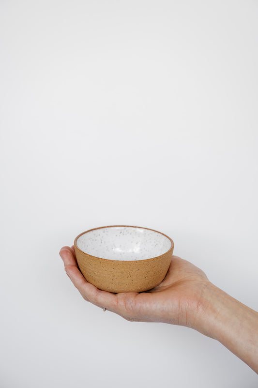 Hand holding a small ceramic bowl with a white interior against a light background showing size and shape. Small-batch pottery Vancouver Island, Canada.