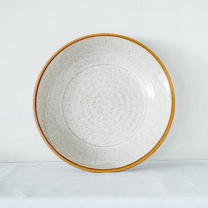 A large Good Wheel Ceramics serving bowl with a speckled white glaze and a contrasted raw brown rim, displayed standing vertically on the rim against a neutral background.