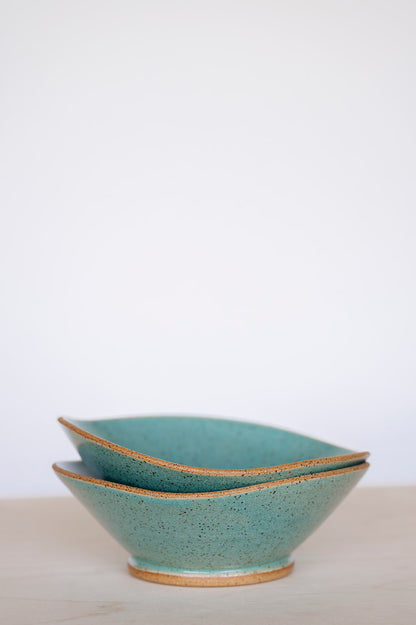 Two stacked, handcrafted ceramic bowls with speckled jaded glaze and raw tan edges, set against a soft, neutral background, conveying a serene and minimalist tone.