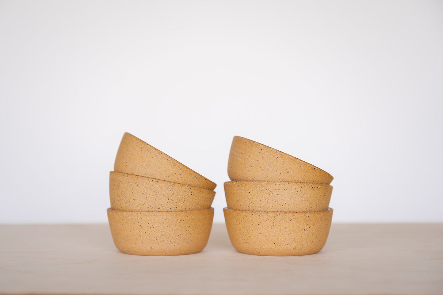 A close up shot of two stacks of three Good Wheel Ceramics Snack bowls on a light surface with a white background. It shows the outside raw speckled clay and texture. 