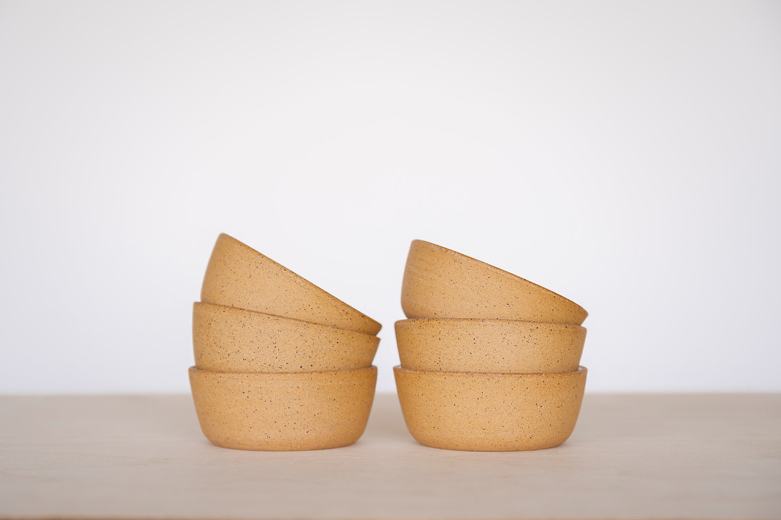 A close up shot of two stacks of three Good Wheel Ceramics Snack bowls on a light surface with a white background. It shows the outside raw speckled clay and texture. 