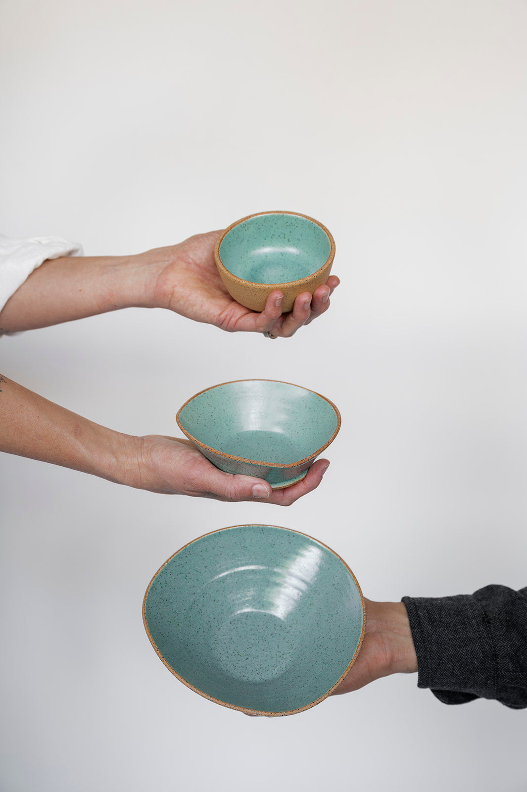 Three hands holding three different Good Wheel Ceramics bowls against a white background. Shows the unique shapes of the handmade bowls made on Vancouver Island, Canada. 