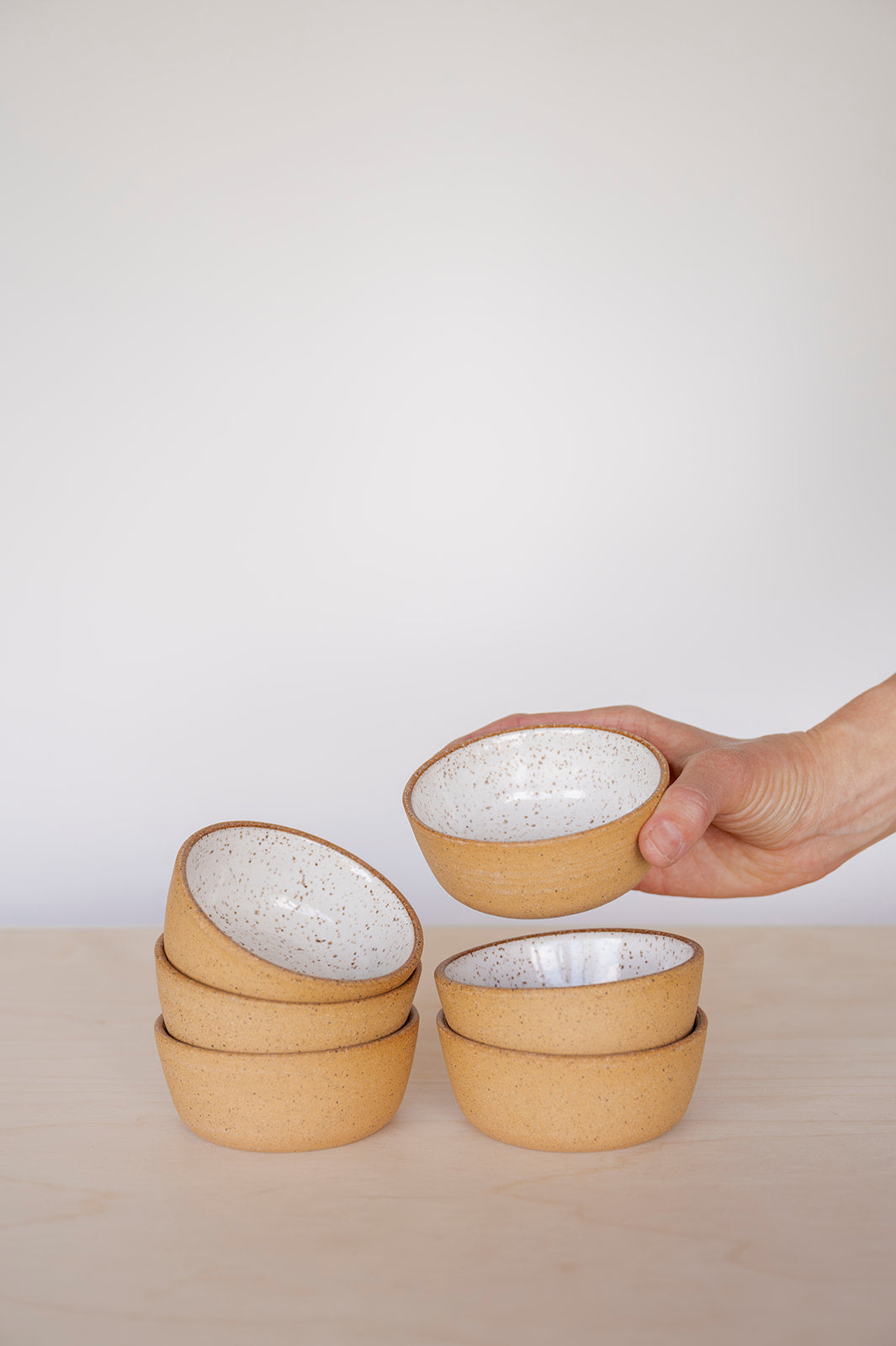 Set of Good Wheel Ceramics Speckled White Snack bowls with a hand holding one, on a light surface with a white background.