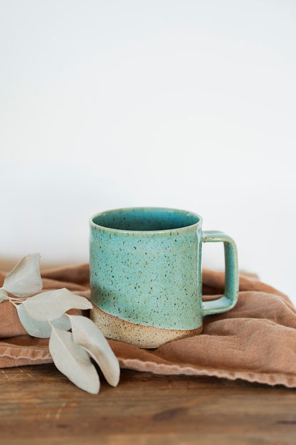 Handmade ceramic mini-barrel mug in speckle jaded glaze on a wooden surface with a burnt orange cloth and dried leaves. 
