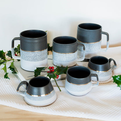 Set of ceramic mugs with black and white design on a wooden surface with a white background