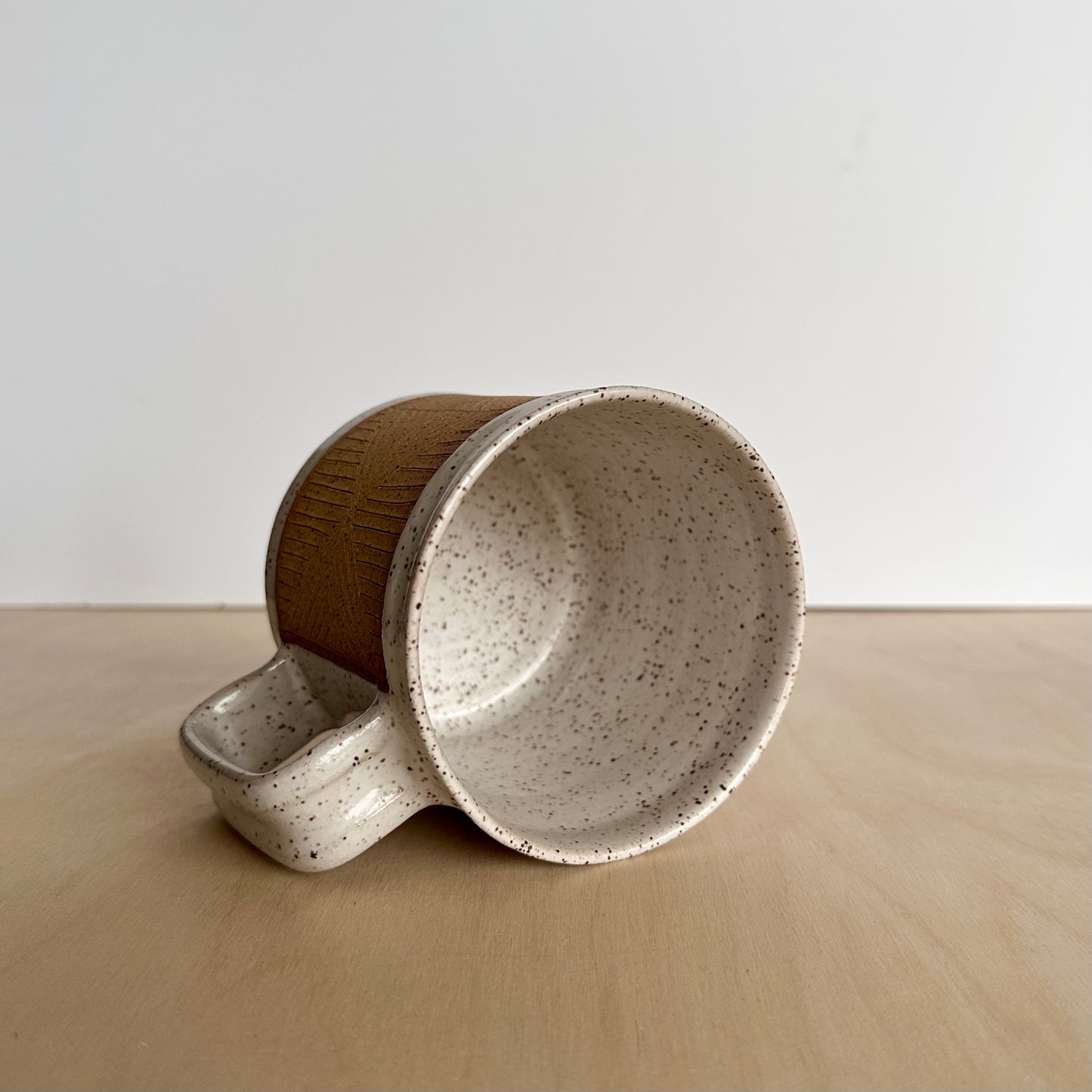 Ceramic mug with hand-carved geometric design sitting on its side on a wooden surface, showing the white glazed inside. 