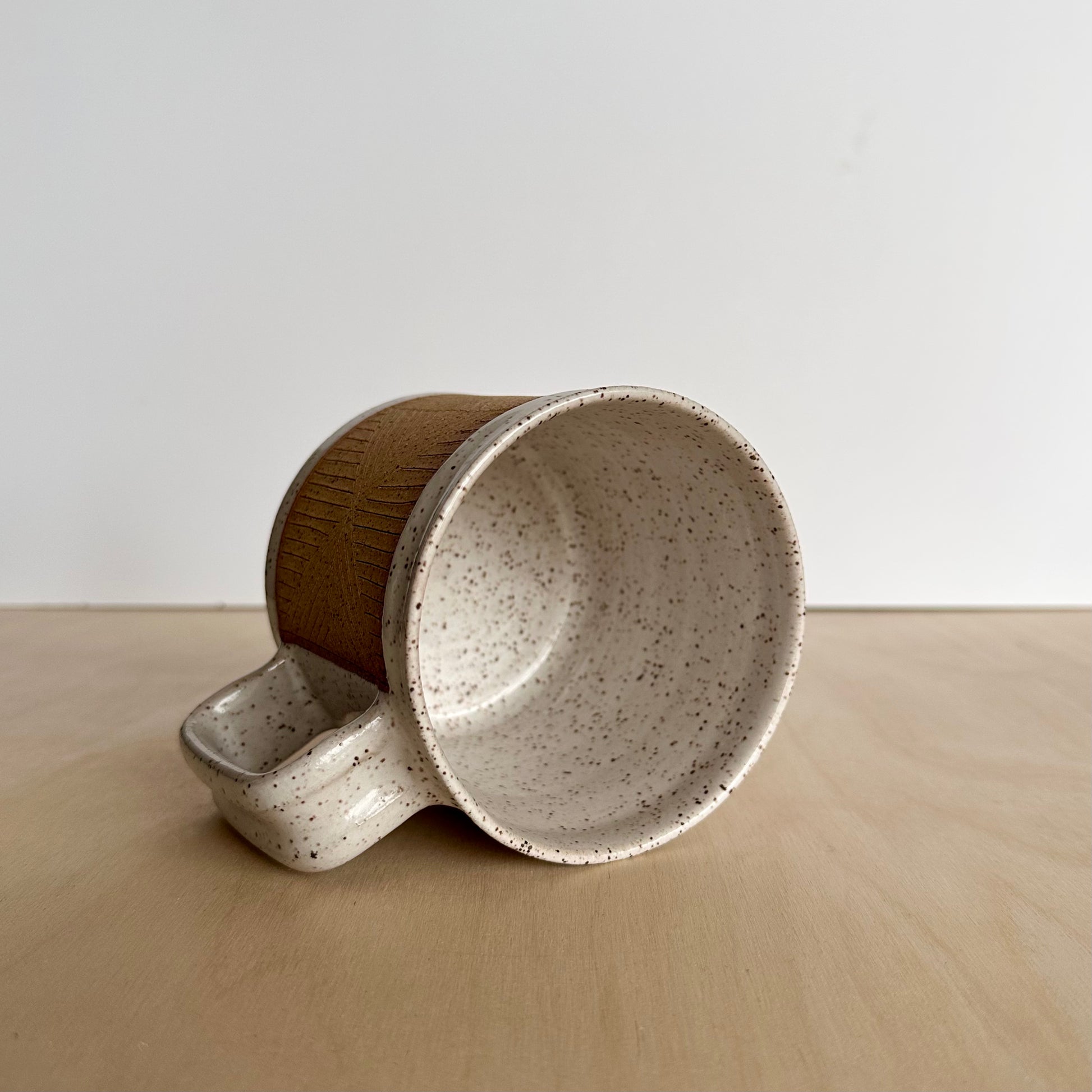 Ceramic mug with hand-carved geometric design sitting on its side on a wooden surface, showing the white glazed inside. 
