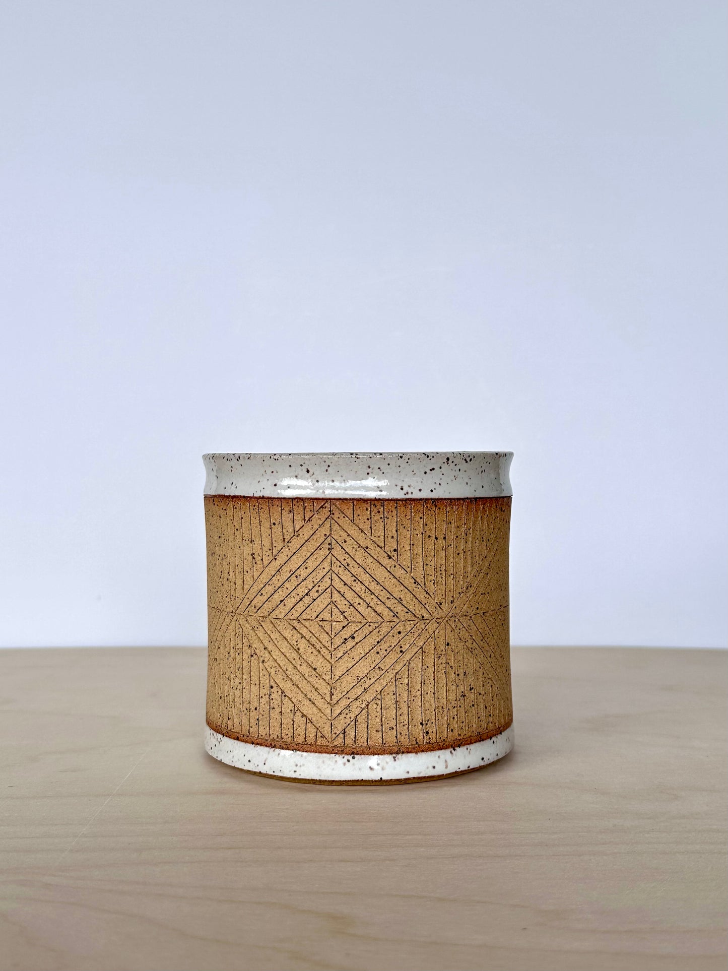 Close up of handmade wheel-thrown ceramic mug with hand-carved diamond pattern. 