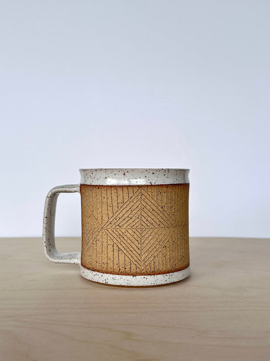Ceramic mug with hand-carved geometric design sitting on a wooden surface, handle facing left. 