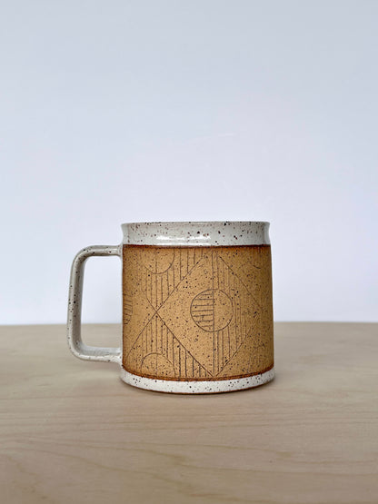 Ceramic mug with unique circles and lines hand-carved geometric design sitting on a wooden surface, handle facing left. 