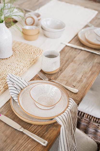 Rustic wooden table setting with speckled white Good Wheel Ceramics dinnerware, tumbler and vase. Neutral tones create a cozy, inviting atmosphere.