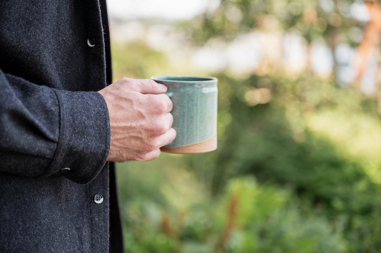 Person holding a green mug outdoors with blurred greenery in the background
