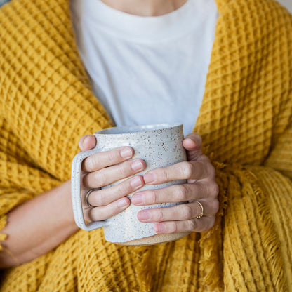 Person wrapped in a yellow blanket holding a ceramic mug