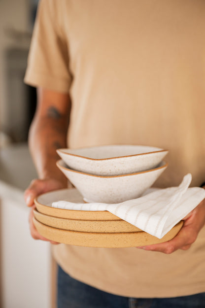 A person holds a stack of Dinner Plates and Triangle Bowls white striped dish towel.